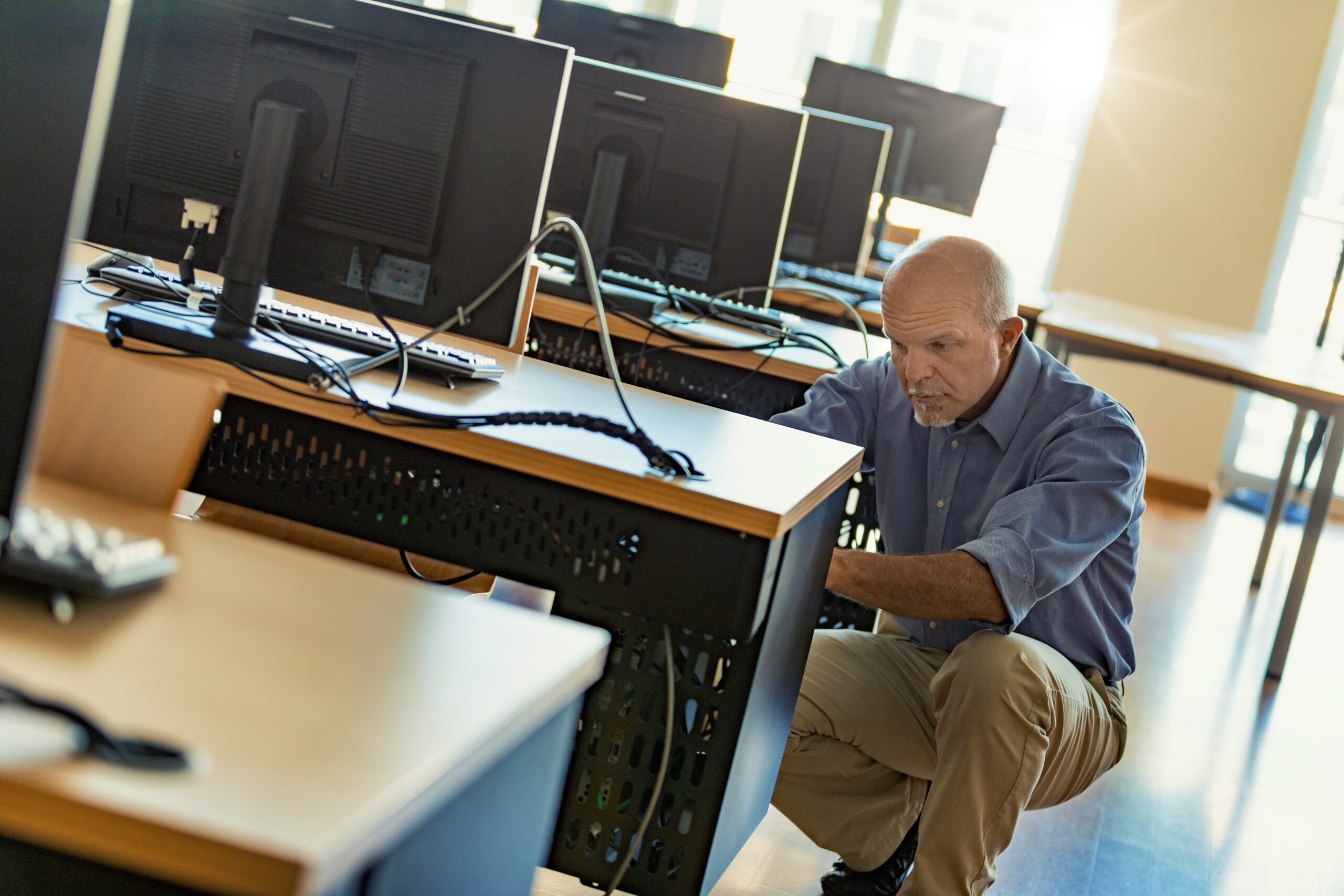 Senior Technician engaged in the physical maintenance of a desktop computer or workstation in a multi-person room, solving problems before they arise.