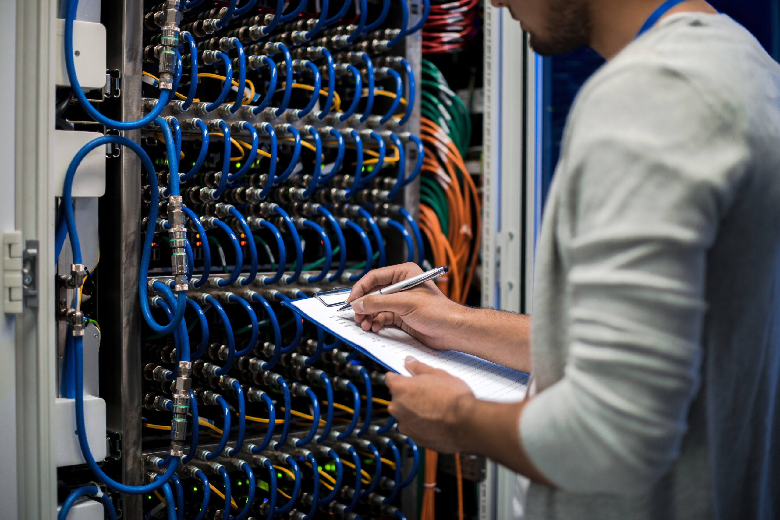 Closeup portrait of young man writing on clipboard  standing by blade server cabinets in research center